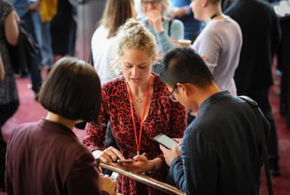 Three people speak in a small group at a work event, one is wearing a lanyard.