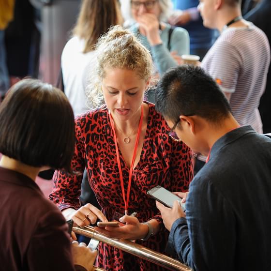 Three people speak in a small group at a work event, one is wearing a lanyard.