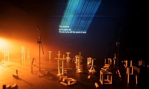 Warm light floods a dark stage with lots of wooden blocks stacked and piled