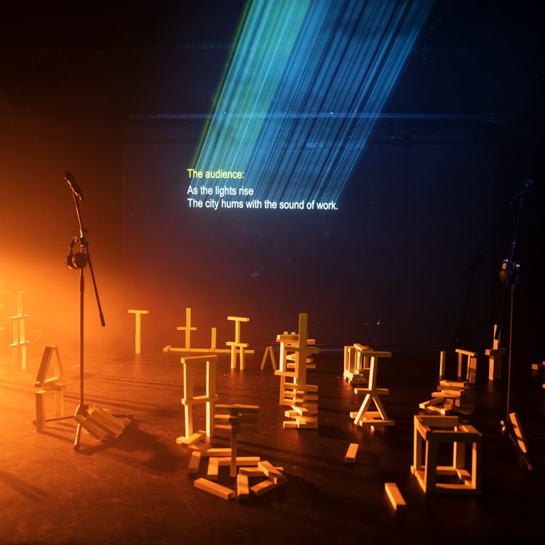Warm light floods a dark stage with lots of wooden blocks stacked and piled
