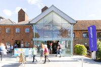 The outside of a large brick building with a glass entrance and a purple 'Farnham Maltings' sign