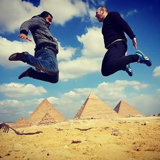 Two people jump in the air with Egyptian Pyramids in the background