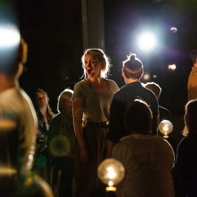 A crowd in a dark room, a woman in open-mouth exclamation is outlined by a halo of light